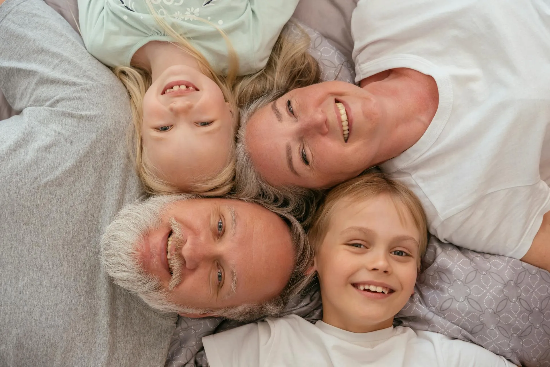 Photo of a family man and woman with young kids maybe 7-8 years old circled around smiling at them camera all lying down looking up