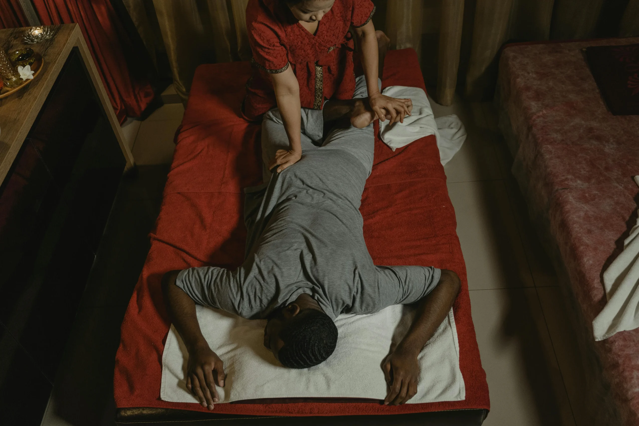 photo of woman doing traditional thai massage on a man stretching leg